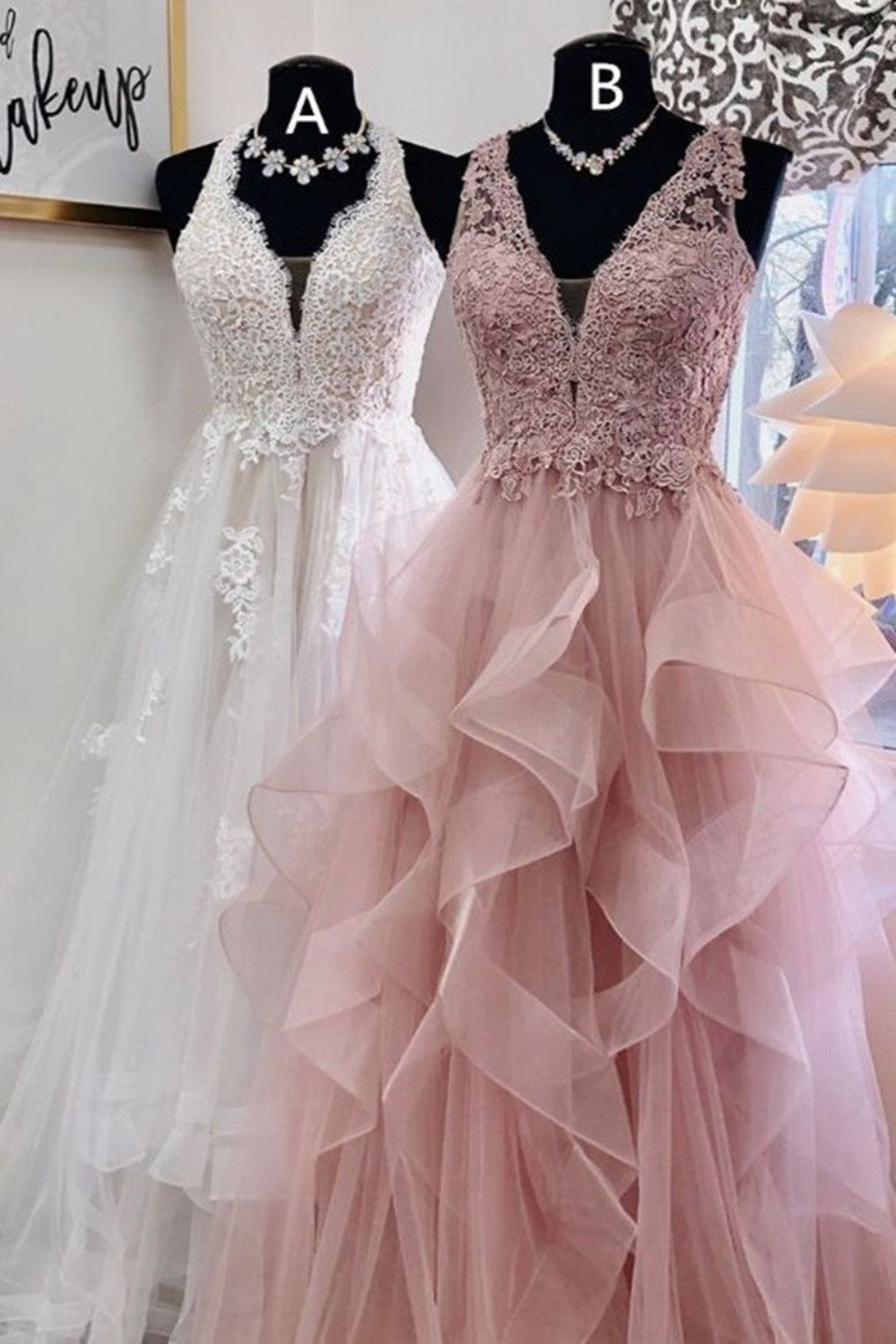 Two prom dresses on display, one in white and one in pink, with v-neck necklines and layered tulle designs.