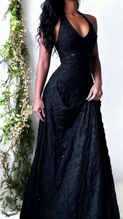 Black lace evening gown worn by a person against a white wall with decorative greenery.